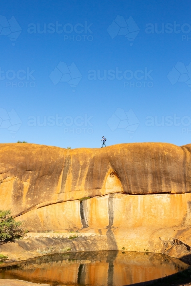 man walking across rock above a natural pool of water - Australian Stock Image
