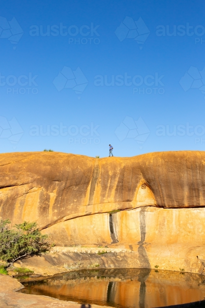 man walking across rock above a natural pool of water - Australian Stock Image