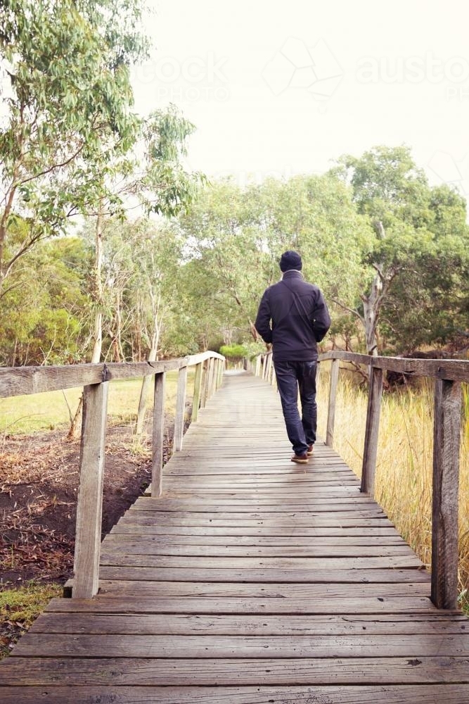 Man walking away along a wooden footbridge in Victorian bushland - Australian Stock Image