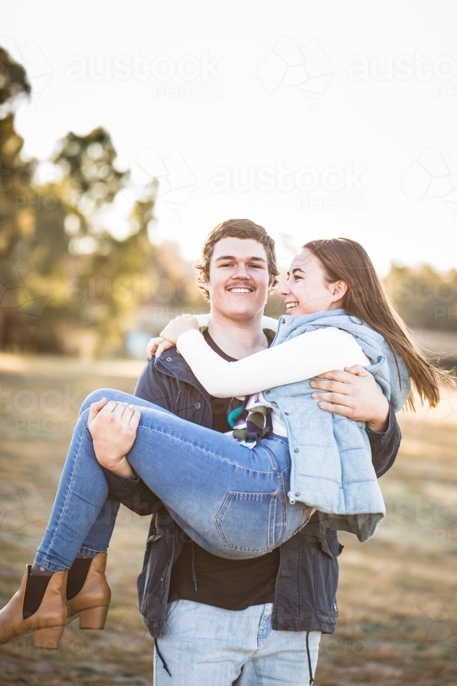 Man walking carrying girlfriend in his arms smiling - Australian Stock Image