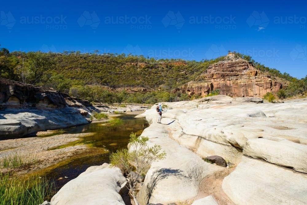 Man walking in a gorge landscape towards rock formation - Australian Stock Image