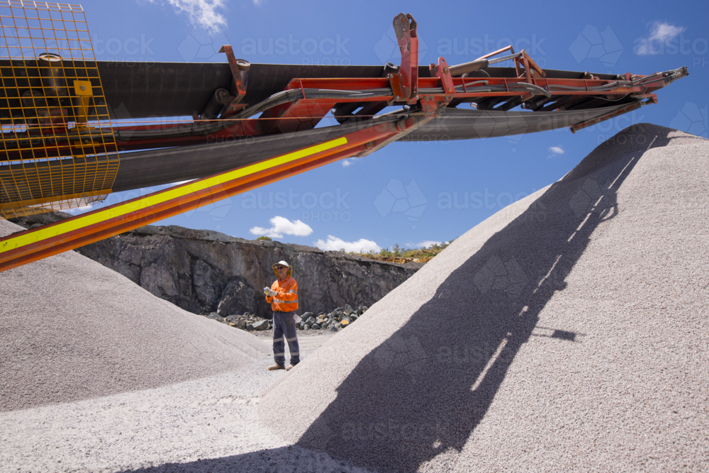Man walking in between piles of aggregates near the crusher. - Australian Stock Image