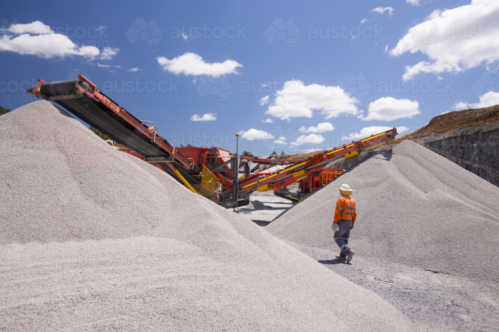 Man walking in between piles of aggregates near the crusher. - Australian Stock Image