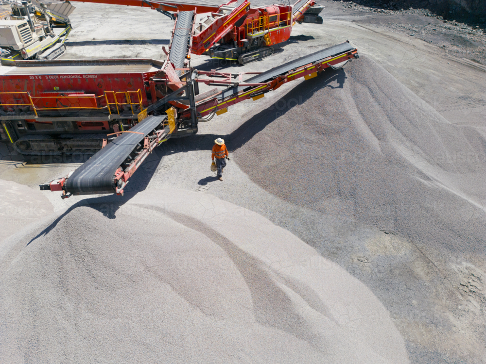 Man walking in between two piles of aggregates from the conveyor belt. - Australian Stock Image