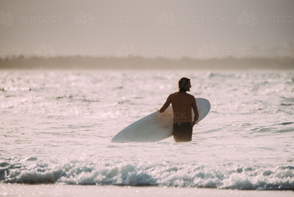 Man walking into the surf at sunset - Australian Stock Image
