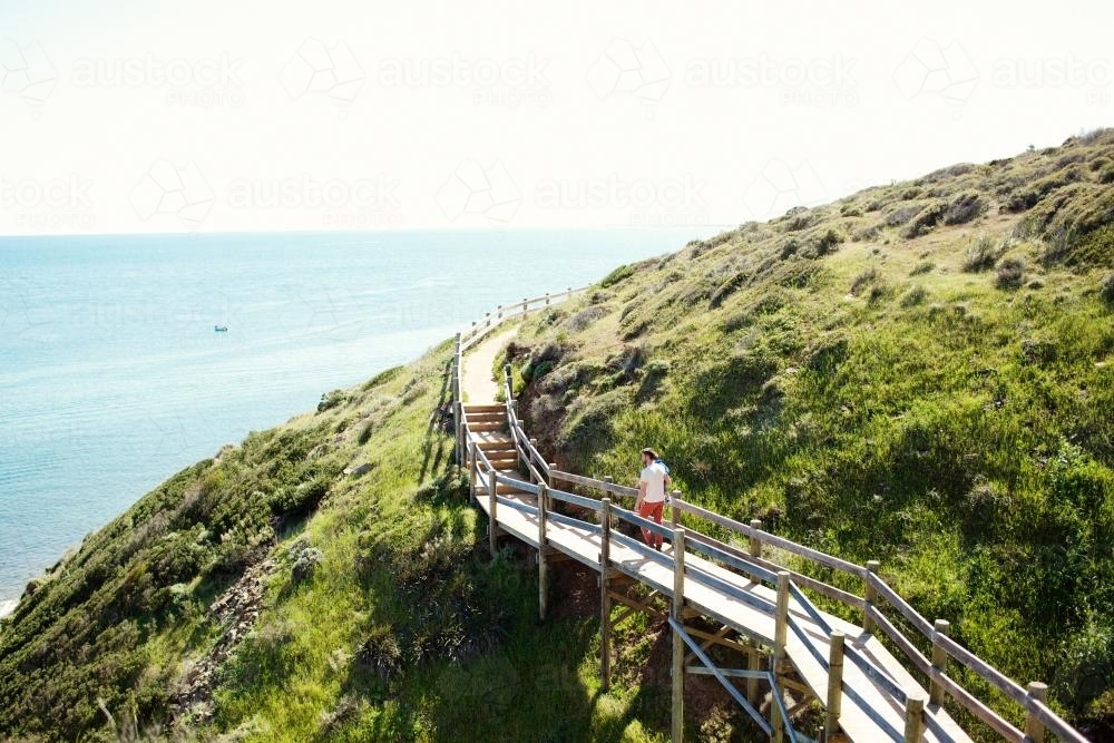 Man walking on a walkway over a mountain on the coast - Australian Stock Image