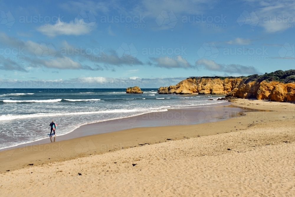 Man walking out to surf at a surf beach - Australian Stock Image