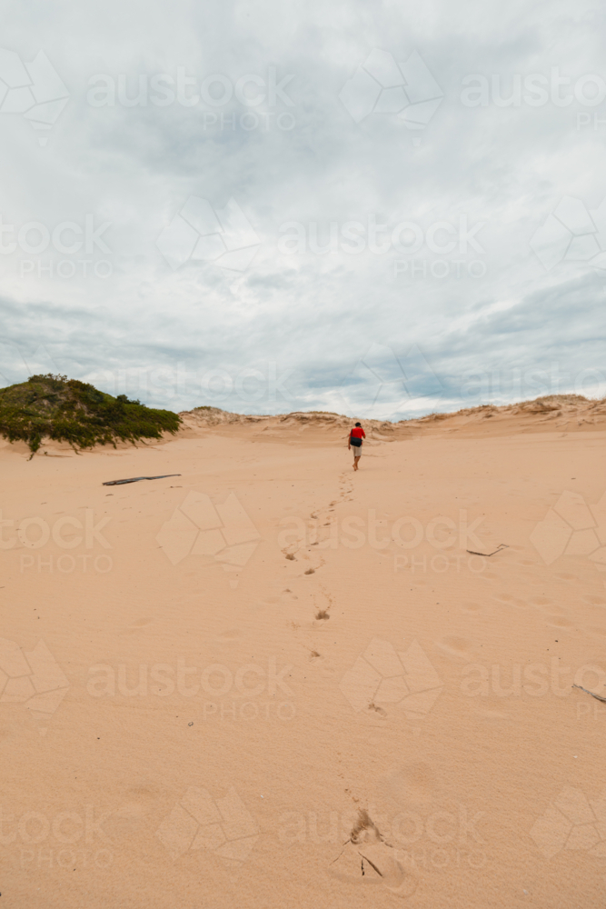 Man walking over sand dunes at Mungo Beach on the NSW coast - Australian Stock Image
