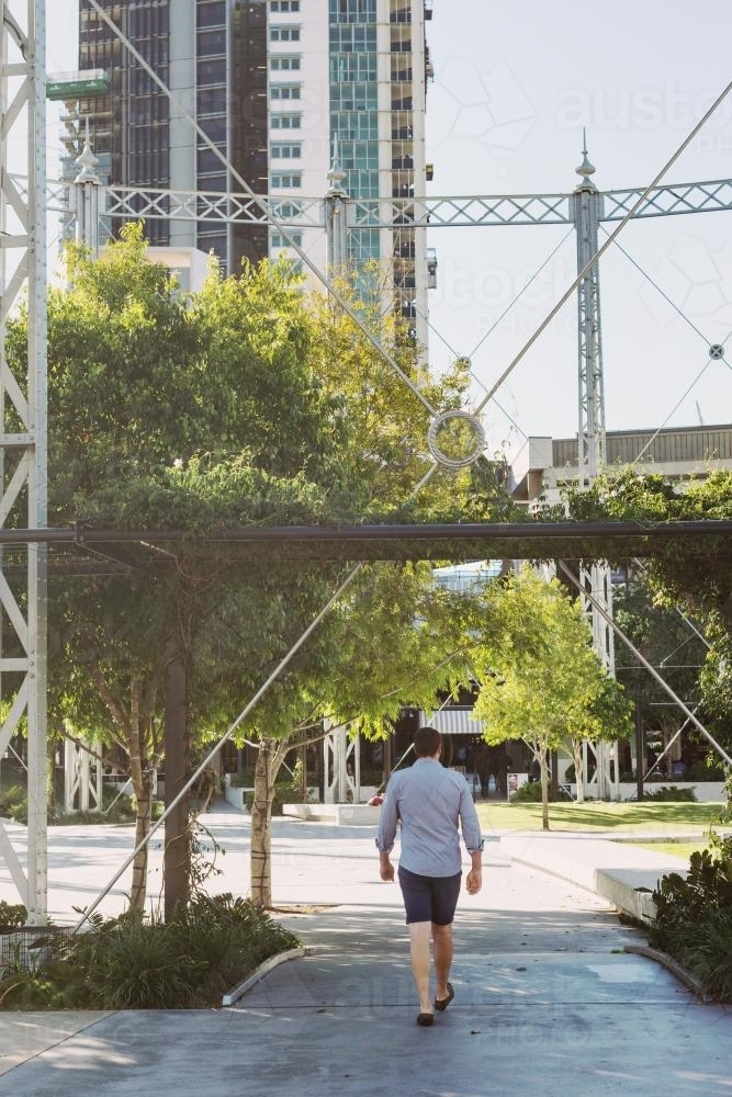 Man walking under a large structure in a city urban park - Australian Stock Image