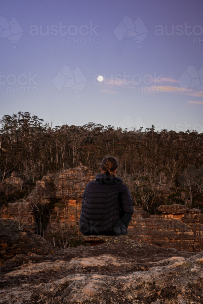 Man watching moon sitting on mountain cliff - Australian Stock Image