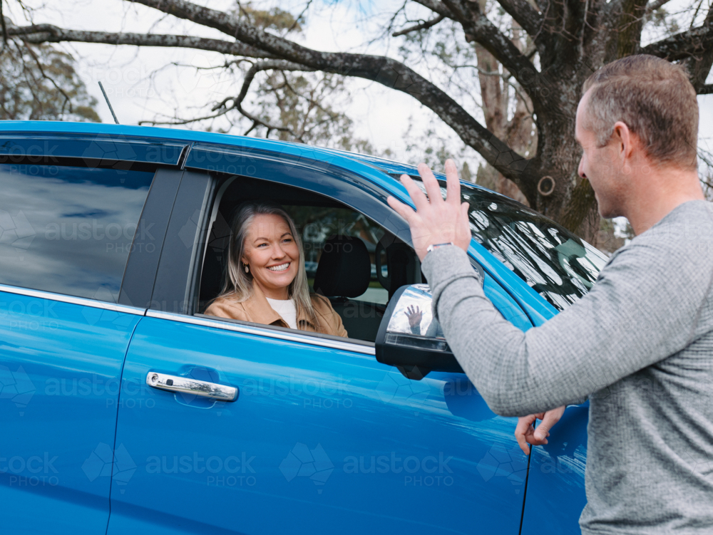 Man waving at a woman on passenger seat of a blue car - Australian Stock Image