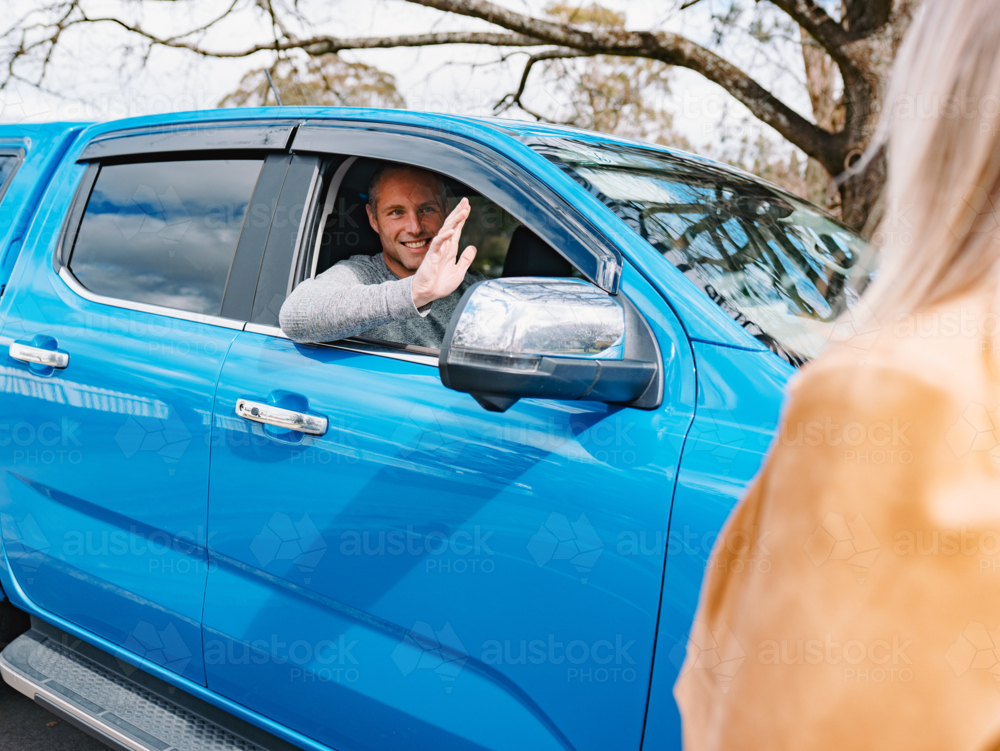 Man waving hand inside the blue car to woman standing outside - Australian Stock Image