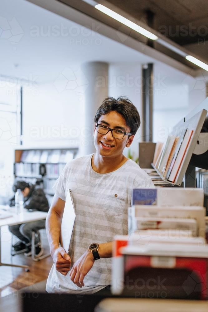 Man wearing glasses with striped t-shirt holding a book in the library - Australian Stock Image