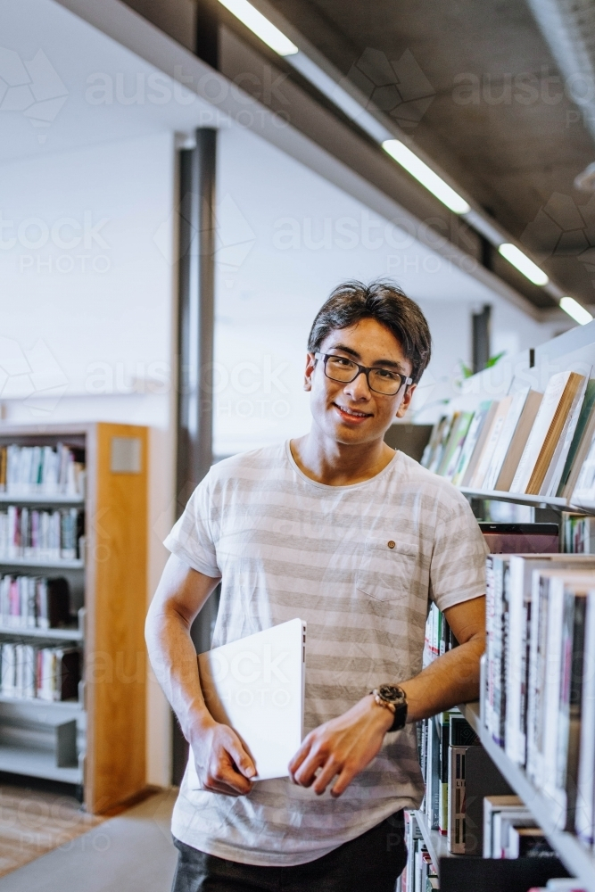 Man wearing glasses with striped t-shirt holding a book in the library - Australian Stock Image