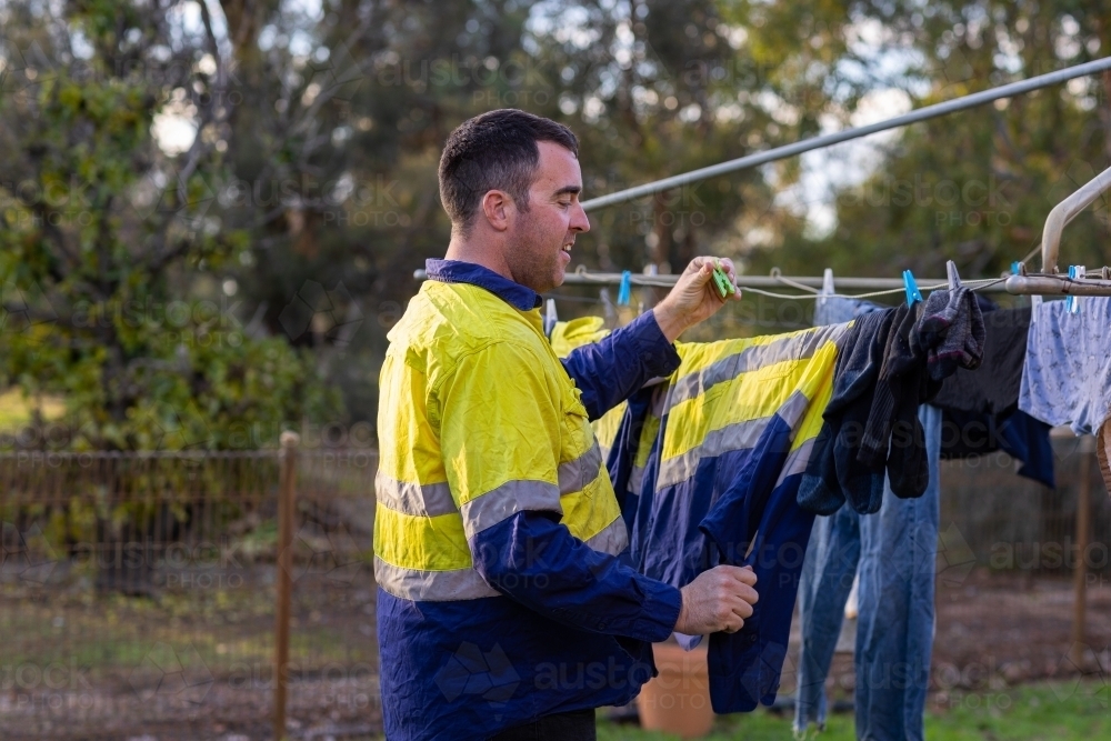 man wearing hi-vis work shirt hanging washing on line on rural property - Australian Stock Image