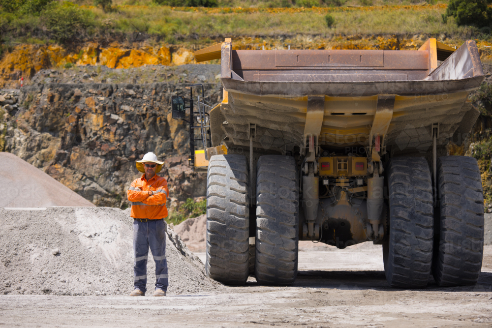 Man with arms crossed standing behind the hauler truck with massive wheels. - Australian Stock Image