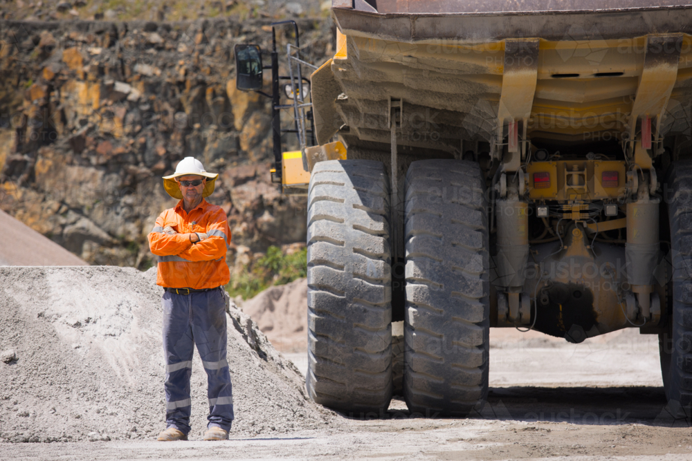 Man with arms crossed standing behind the hauler truck with massive wheels. - Australian Stock Image
