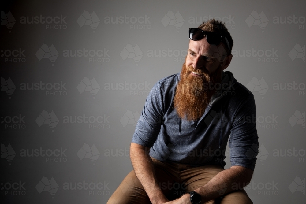 Man with beard and sunglasses sitting and smiling. - Australian Stock Image