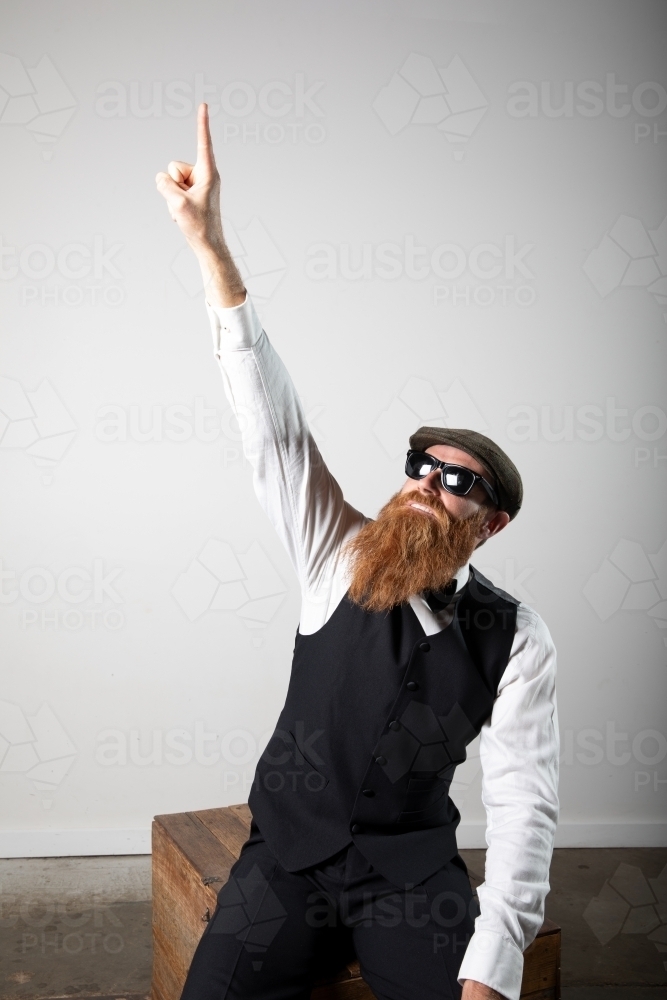 Man with ginger beard and tweed flat cap sitting, posing. - Australian Stock Image