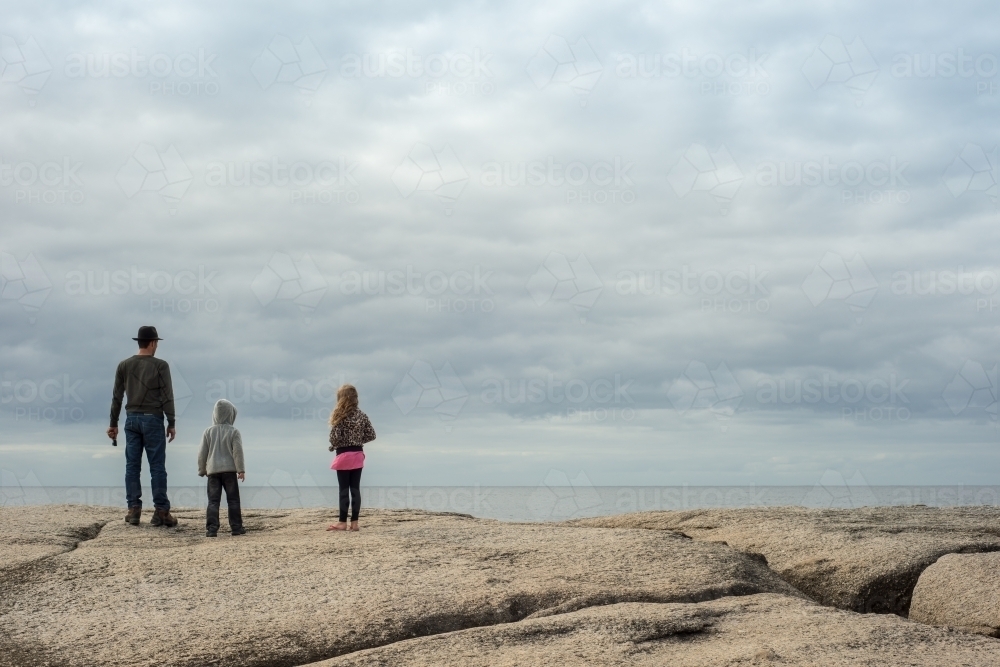 Man with girl and boy on boulder rocks at beach - Australian Stock Image