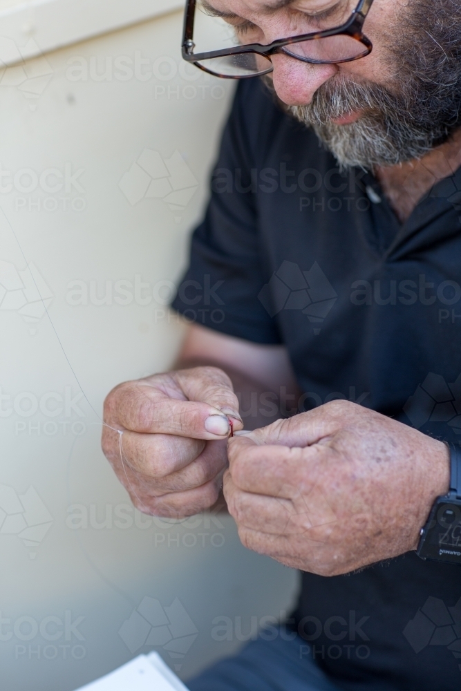 Man with glasses threading fishing hook - Australian Stock Image