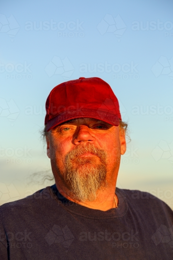 Man with a goatee beard in maroon cap, looking at camera.. - Australian Stock Image