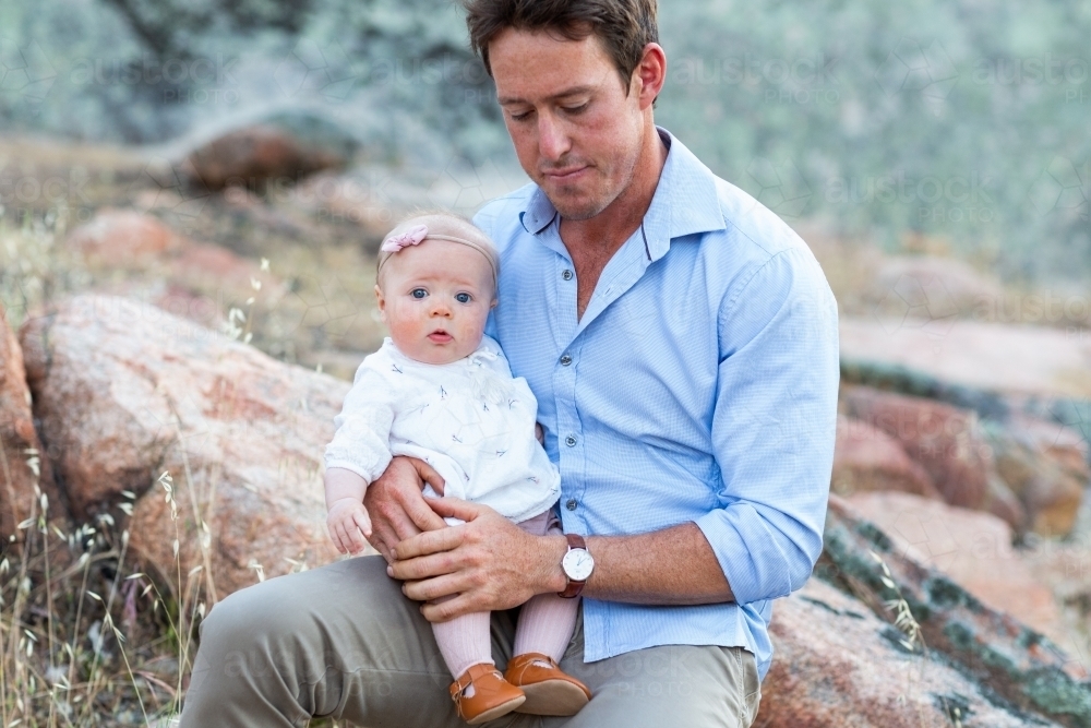 Man with his baby girl on his lap outdoors - Australian Stock Image