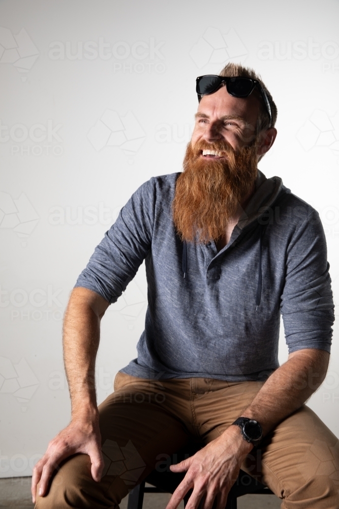 Man with long beard and sunglasses seated and smiling - Australian Stock Image