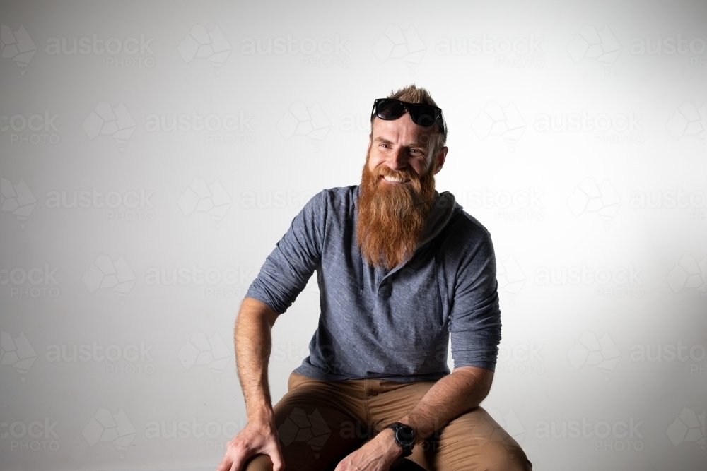 Man with long beard and sunglasses seated and smiling - Australian Stock Image
