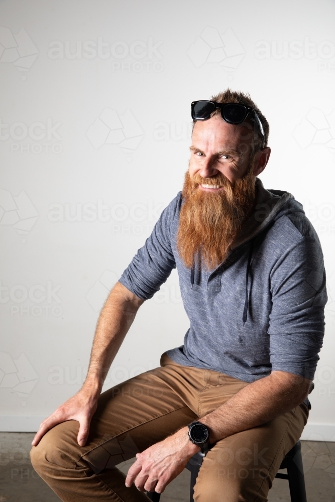 Man with long beard and sunglasses seated and smiling - Australian Stock Image