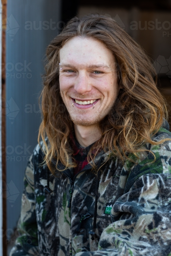 Man with long hair and piercings smiling - Australian Stock Image