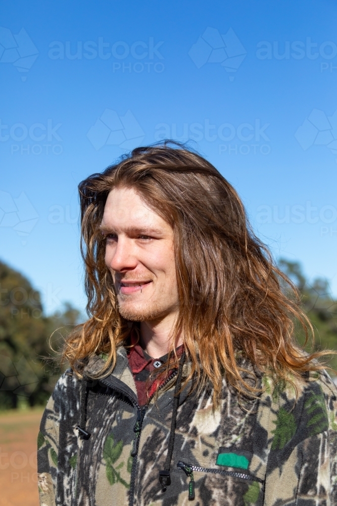 Man with long hair looking into the distance outdoors - Australian Stock Image