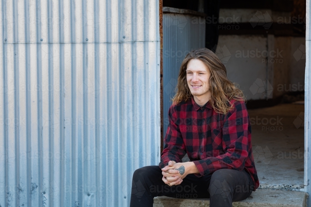 man with long hair sitting on the steps of a shearing shed - Australian Stock Image