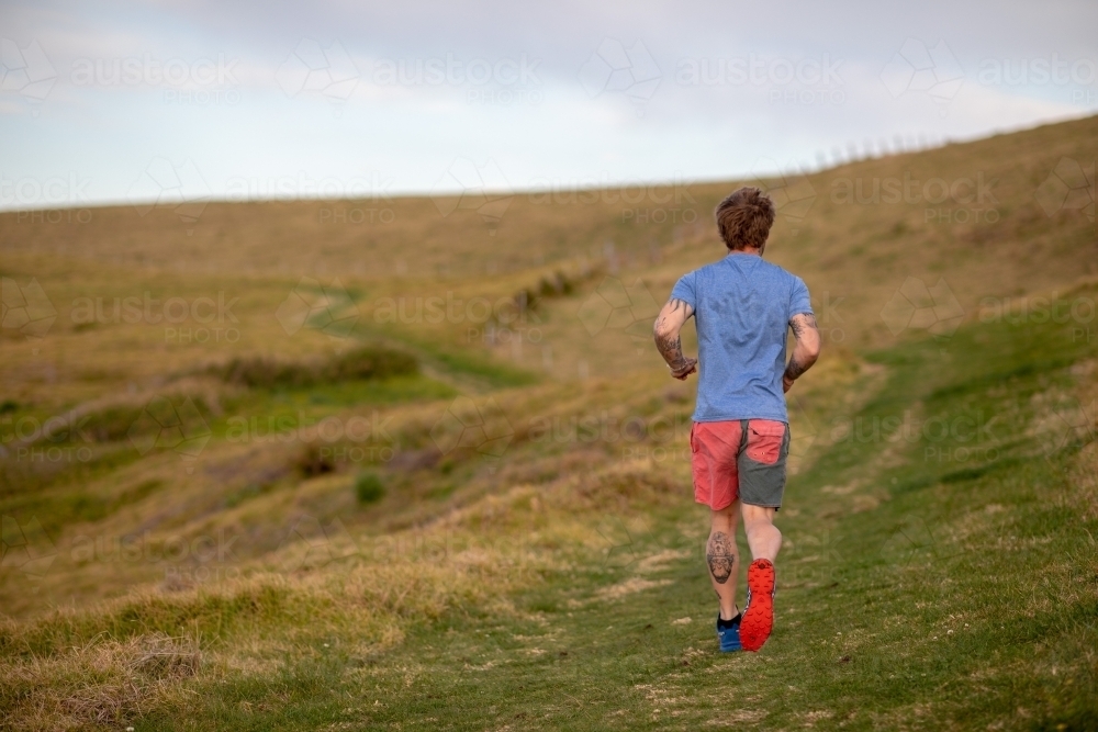 Man with Tattoo Running Alone in Countryside - Australian Stock Image