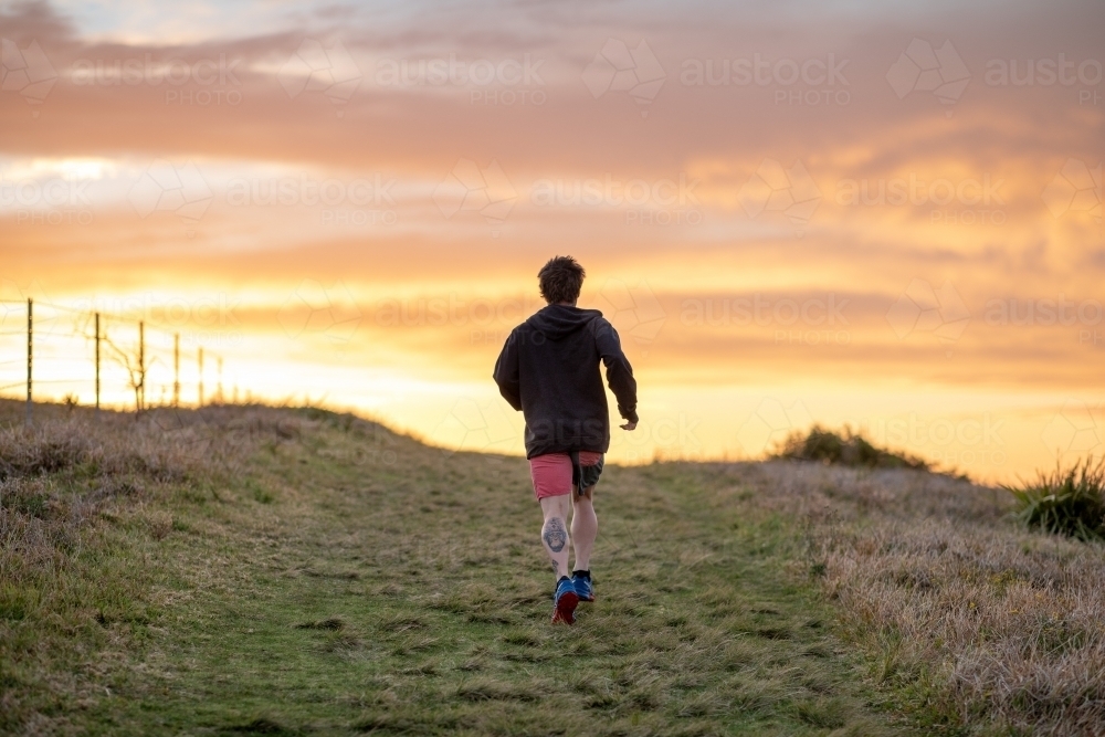 Man with Tattoo Running Uphill Towards Sunrise - Australian Stock Image