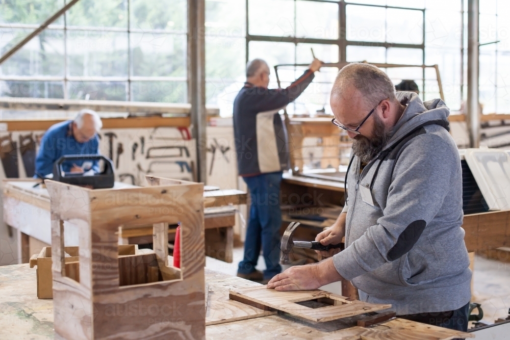 Man working at a Men's shed with men in background - Australian Stock Image