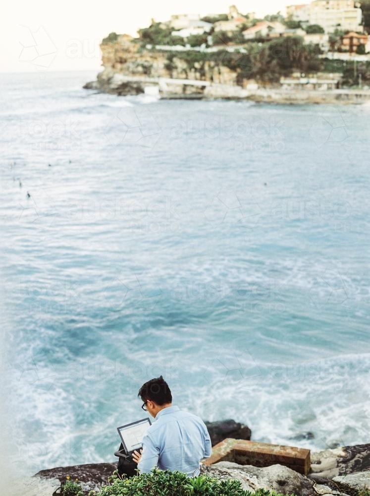 Image of Man working on a laptop computer overlooking the ocean ...