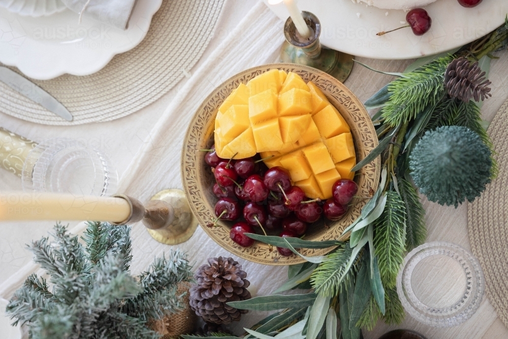 Mango and cherries in bowl on decorated Christmas table - Australian Stock Image