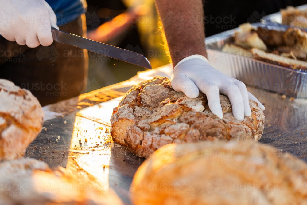 Mans hands cutting camp oven damper bread with knife - Australian Stock Image