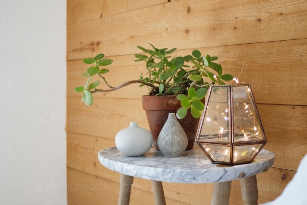 Marble bedside table against timber wall with vases, indoor plant and lantern - Australian Stock Image