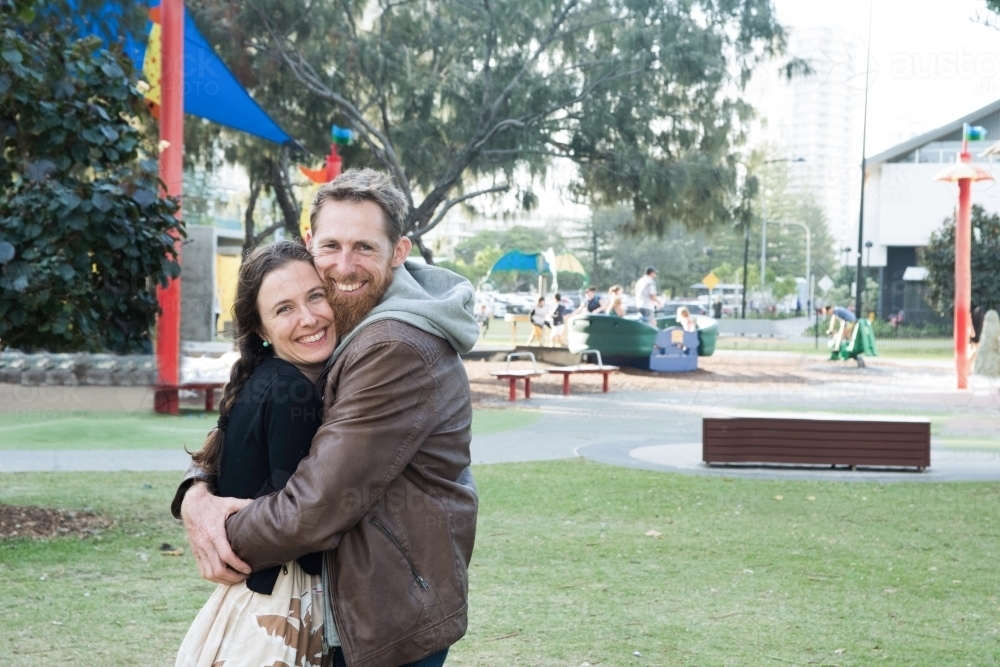 Married couple hugging tightly while smiling at the camera at the park. - Australian Stock Image
