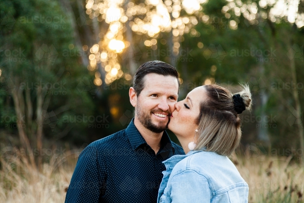 Married couple wife kisses husband in park - Australian Stock Image