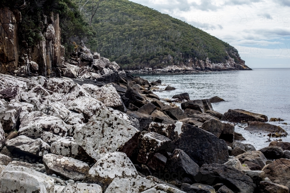 Massive boulders covered in white lichen line the coast  as Cape Hauy rises in the background - Australian Stock Image