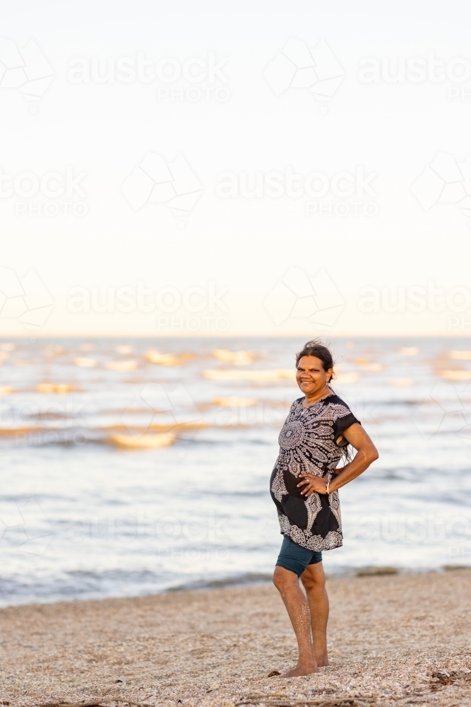 mature aboriginal woman standing on beach in vertical format with lots of space above - Australian Stock Image