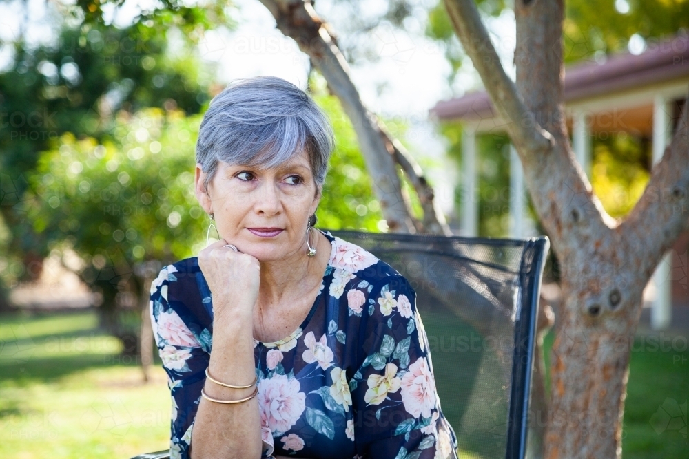 Mature aged woman relaxing in backyard under shady tree - Australian Stock Image