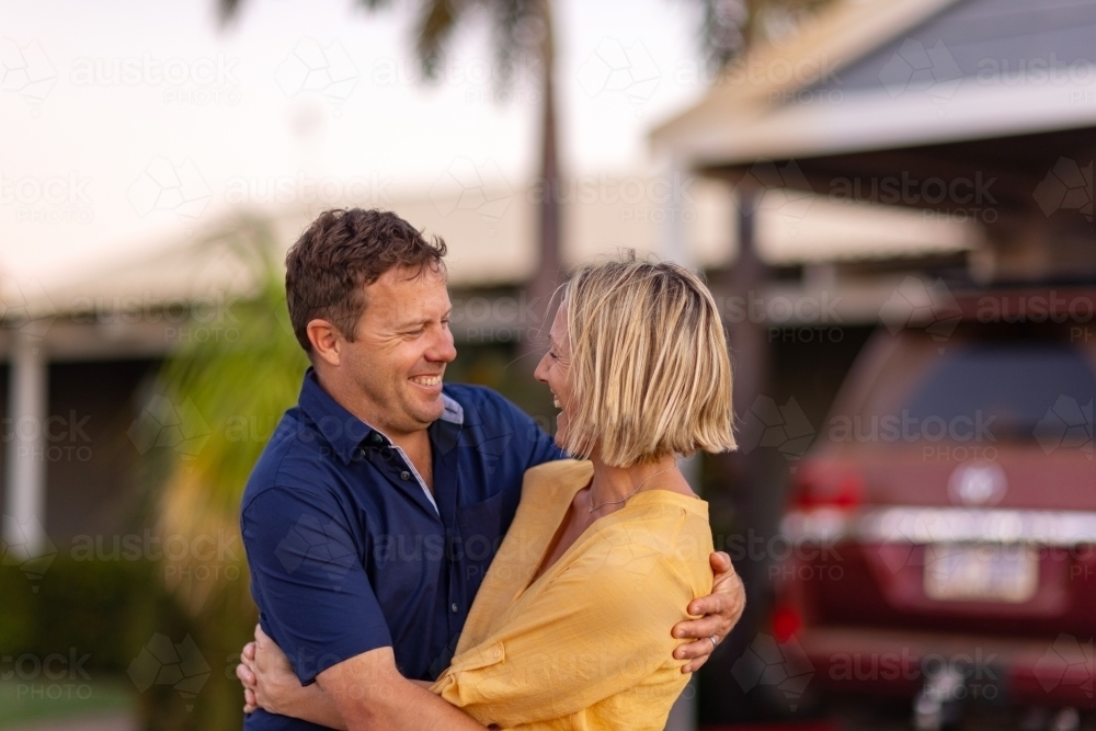 mature couple embracing in front of their home and car - Australian Stock Image