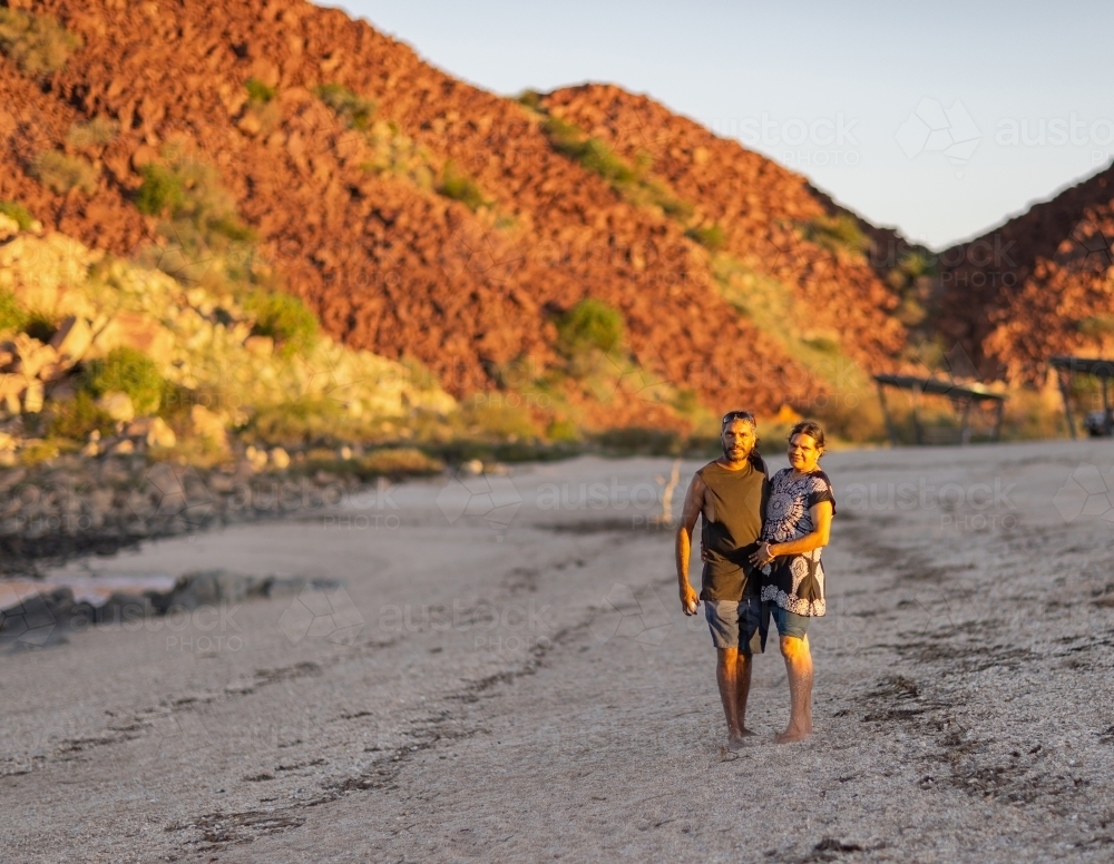mature couple on beach at hearsons cove as sun goes down with red hills lit up by sun - Australian Stock Image