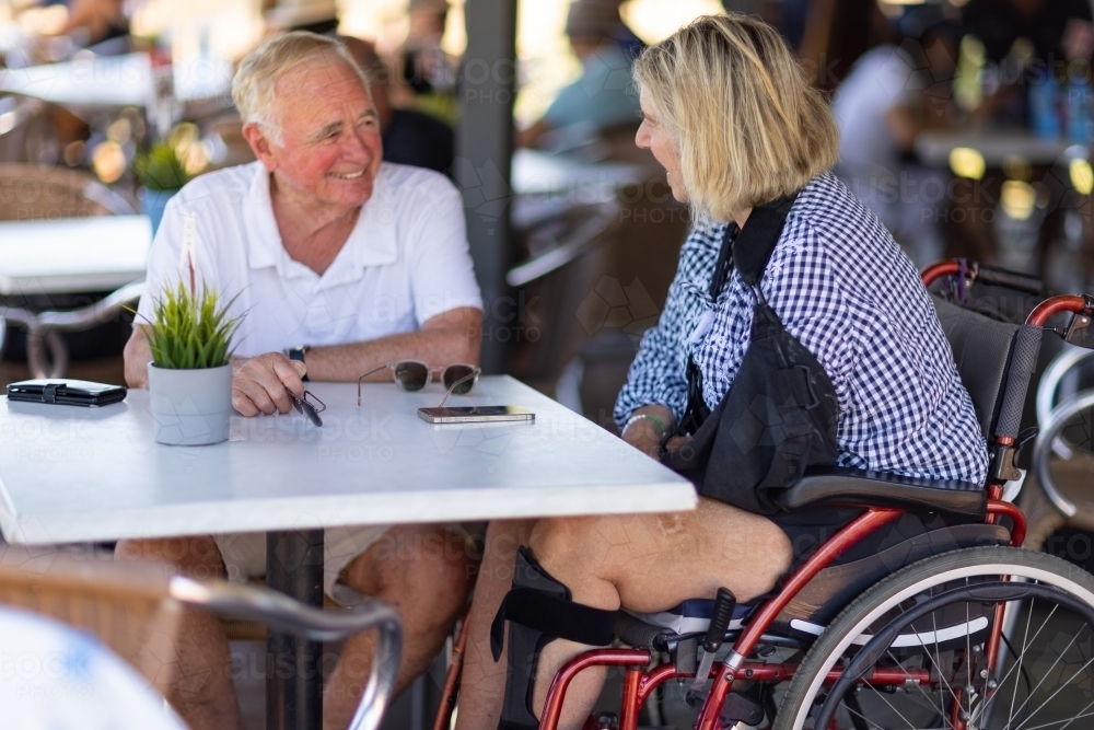 mature couple sitting at cafe table with woman in wheelchair - Australian Stock Image