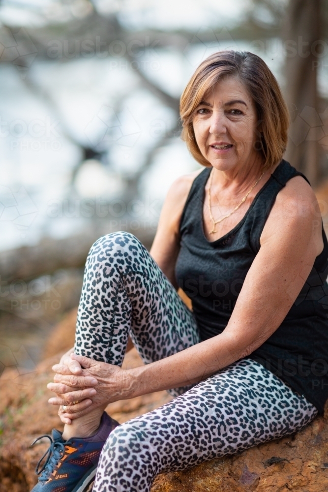 mature lady in activewear sitting in quiet spot by river - Australian Stock Image
