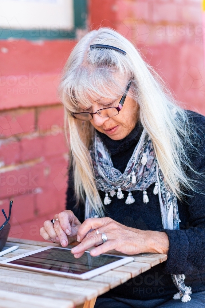Mature lady wearing spectacles typing on a tablet - Australian Stock Image